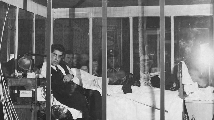 Alfons Kieres w szklanej klatce w trakcie głodówki. Widoczne syfony z wodą sodową.