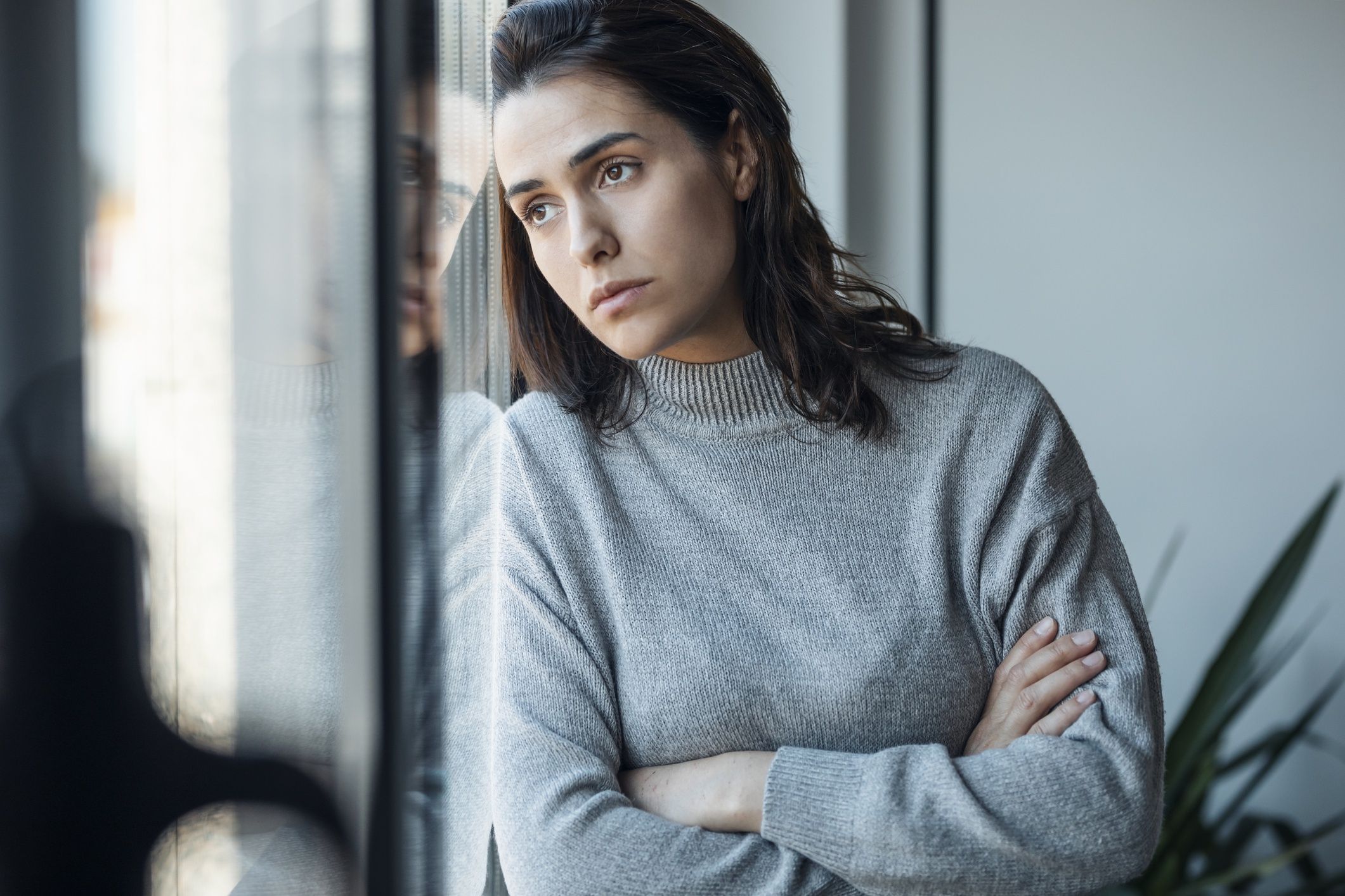 Depressed woman standing with arms crossed looking through window at home
Westend61