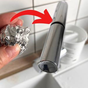 ręka trzymająca kulkę z folii aluminiowej obok kuchennego kranu