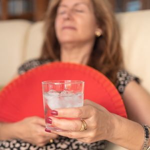 kobieta leży zmęczona na kanapie i trzyma szklankę z wodą