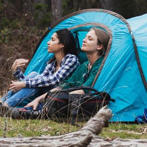 dwie kobiety siedzące na brzegu namiotu w lesie