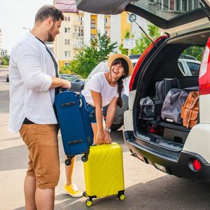 para pakująca walizki do bagażnika auta i kupka pieniędzy