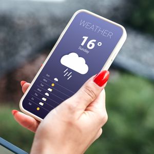 dłoń kobiety z telefonem z otwartą aplikacją pogodową