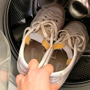ręka wkładająca białe buty do pralki