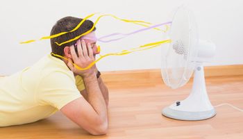 mężczyzna leży przed włączonym klimatyzatorem na podłodze