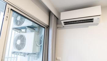 klimatyzator na ścianie mieszkania, a przez okno widać zewnętrzną część instalacji