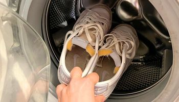 ręka wkładająca białe buty do pralki