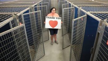 Pracownica schroniska pozuje do zdjęcia wraz z pustymi klatkami i kartką z napisem „Dziękujemy!”