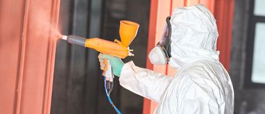 osoba w kombinezonie ochronnym i masce w trakcie malowania proszkowego