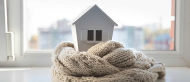 Makieta małego domu otulona szalikiem ustawiona na parapecie okna