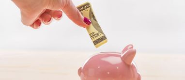 kobieca dłoń wkładająca banknot do świnki-skarbonki