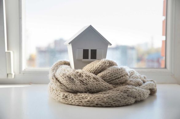 Makieta małego domu otulona szalikiem ustawiona na parapecie okna