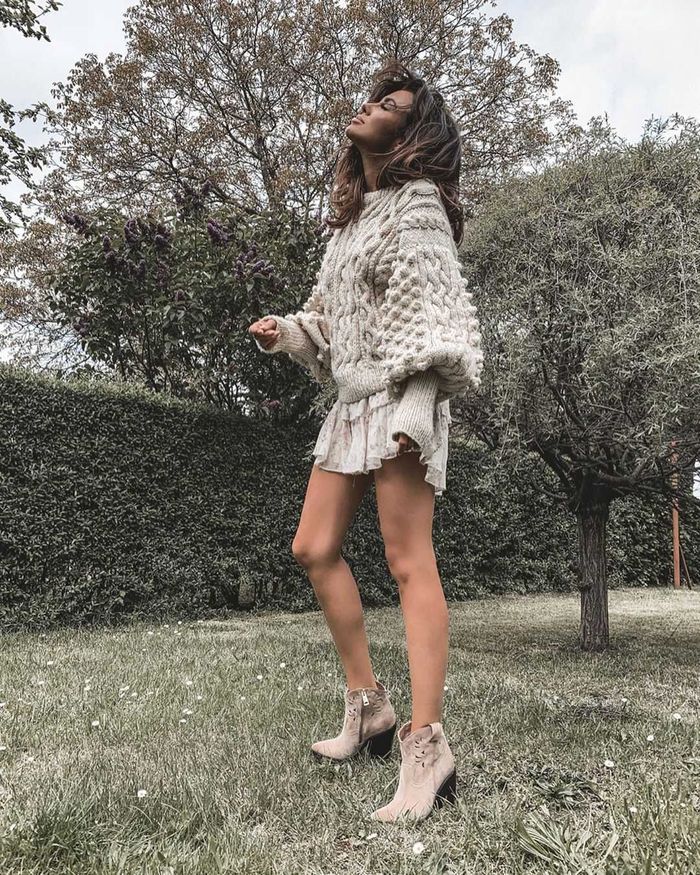 Natalia Siwiec w mini , swetrze oraz kozakach pozuje na łące