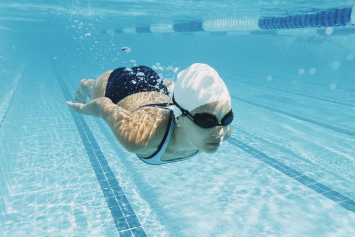 Kobieta w czepku pływająca pod wodą na basenie