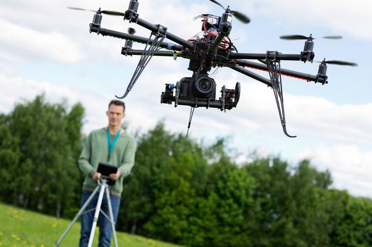 Zdjęcie UAV octocopter flying with technician operating in background at park pochodzi z serwisu Shutterstock