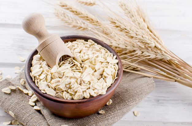 Oat flakes  in ceramic bowl and wooden spoon and spikelets on white vintage wooden background, selective focus copy space, top view