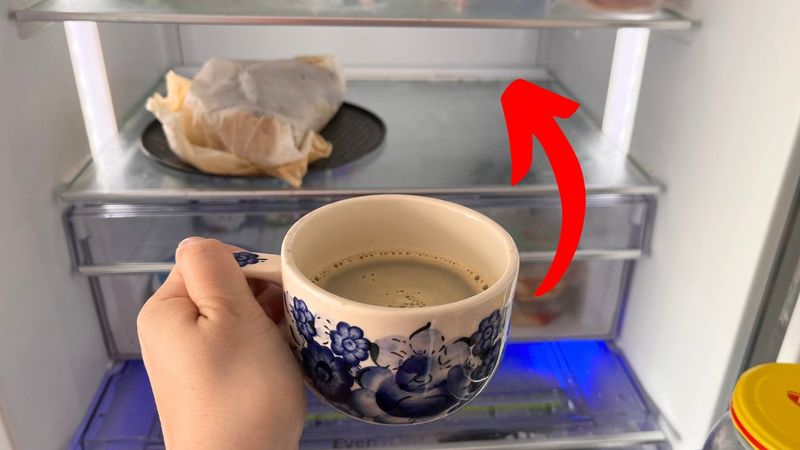 ręka z filiżanką kawy na tle otwartej lodówki