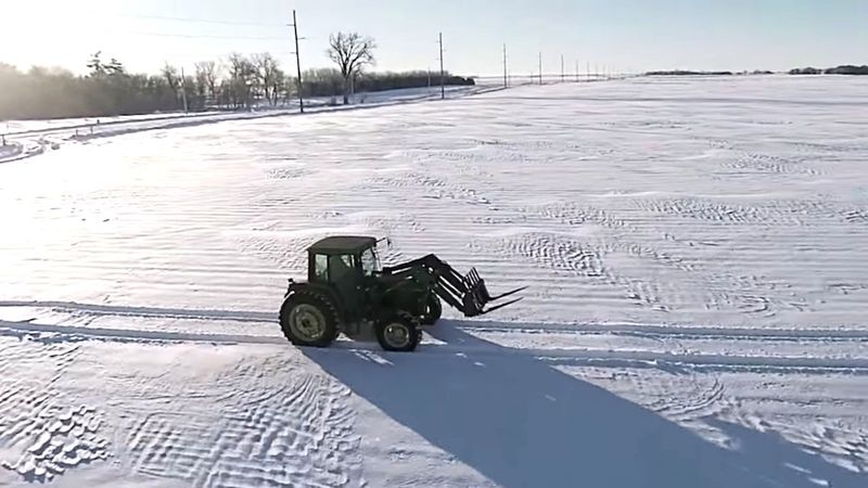 Farmer jedzie ciągnikiem przez pole pełne śniegu. Patrz, co się dzieje, kiedy kamera się oddala