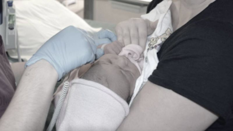 Ojciec mocno przytrzymuje synka. Drugi mężczyzna pochyla się nad chłopcem i wykonuje tatuaż