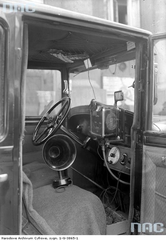 1932
Wnętrze taksówki wyposażonej w radioodbiornik. Widoczna deska rozdzielcza samochodu, radio i głośnik.