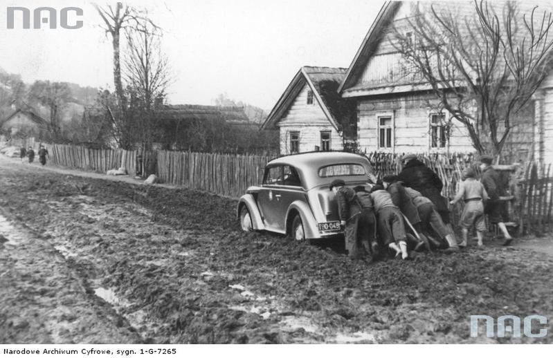 1938
Grupa ludzi pcha samochód po błotnistym Trakcie Kowieńskim