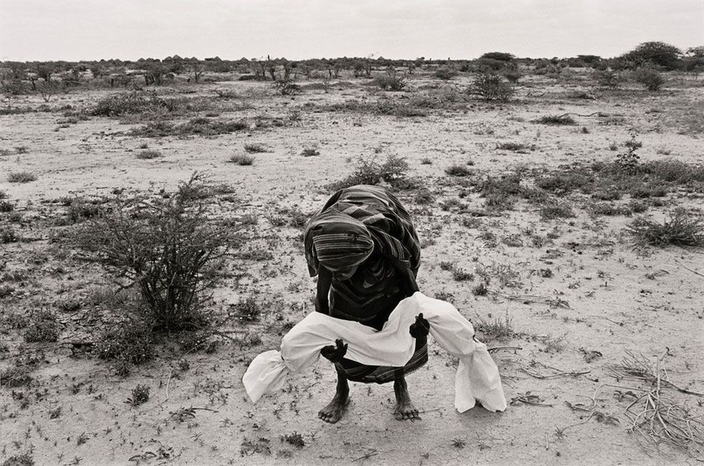 1992 r. Bardera, Somalia. Matka niesie do grobu martwe dziecko zawinięte w całun (zgodnie z miejscowym zwyczajem). Susza i wojna domowa spowodowały straszliwy głód w Somalii. W ciągu dwóch lat życie straciło wtedy 1-2 miliony ludzi. Dostawy humanitarne z międzynarodowego transportu lotniczego, które rozpoczęły się w lipcu, były utrudnione przez ataki silnie uzbrojonych gangów z klanu. Centra żywności plądrowano, co ograniczało pomoc oraz spowalniało dystrybucję żywności przez organizacje humanitarne.
Fot. James Nachtwey, World Press Photo of the Year