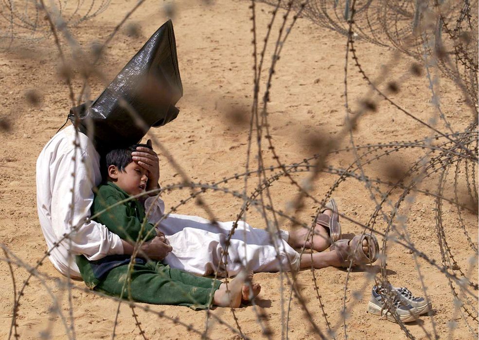 2003 r. Irak. Irakijczyk przytula swojego czteroletniego synka w ośrodku dla jeńców wojennych w obozie bazy US Army 101 Dywizji Powietrznodesantowej w pobliżu Nadżafu. Chłopiec stał przerażony, kiedy jego ojcu założono kaptur i plastikowe kajdanki, które żołnierz później zerwał. Wojskowi twierdzili, że torby zostały użyte, aby zdezorientować więźniów i ochronić ich tożsamość. Nie wiadomo, co stało się z mężczyzną i jego synem.
Fot. Jean-Marc Bouju, World Press Photo of the Year