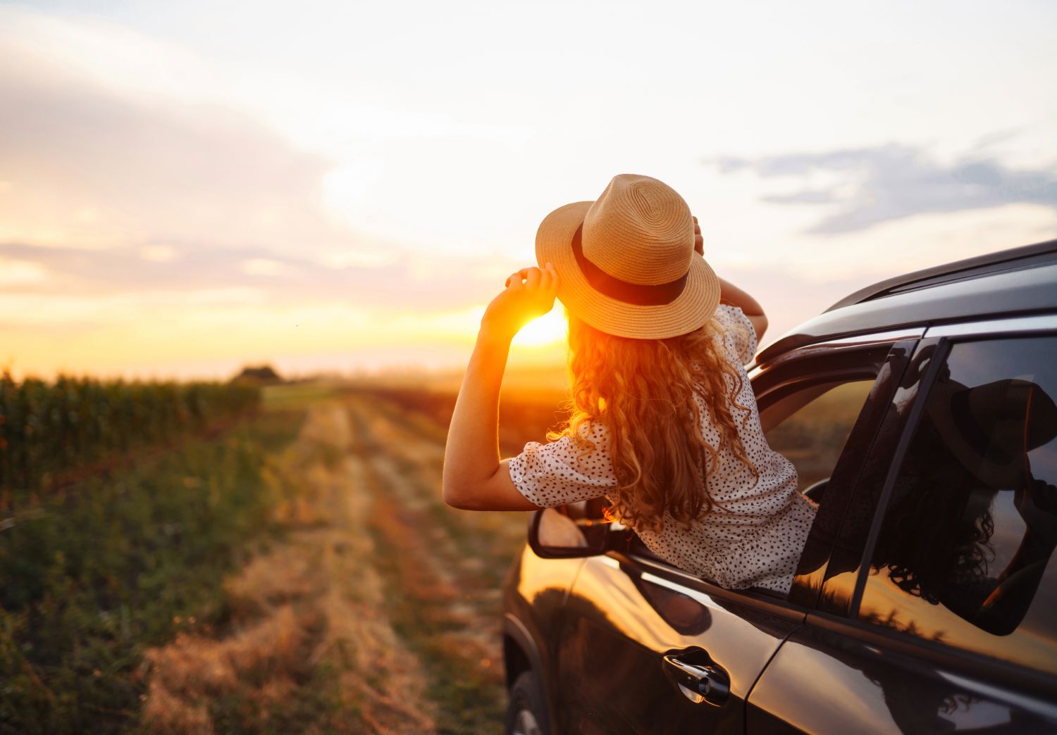 Roadtrip po Polsce - dziewczyna w kapeluszu w samochodzie obrócona plecami patrzy w stronę zachodzącego słońca